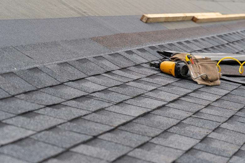 Photo of toolbelt with instrument and nail gun lying on asphalt or bitumen shingle on top of the new roof under construction residential house or building