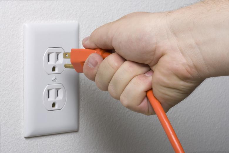 Unplugging an orange cord from a white electrical outlet.