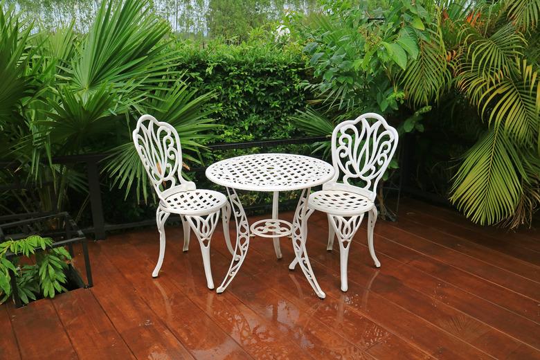 White wrought iron garden tea table and chairs on patio after rain.