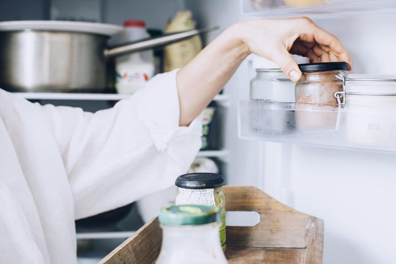 Hand reaching for small food jar inside of fully stocked white refrigerator