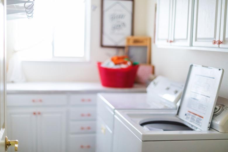 A top-loading washing machine with an open lid inside a laundry room