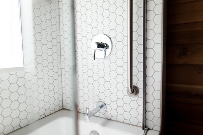 A shower with white hexagon tiles, metal faucet hardware, and glass doors.