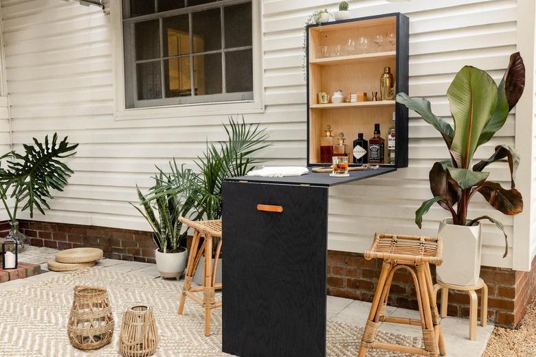 Patio with rattan furniture, black plywood bar table-cabinet set, tropical plants, lanterns, and black-white accents.