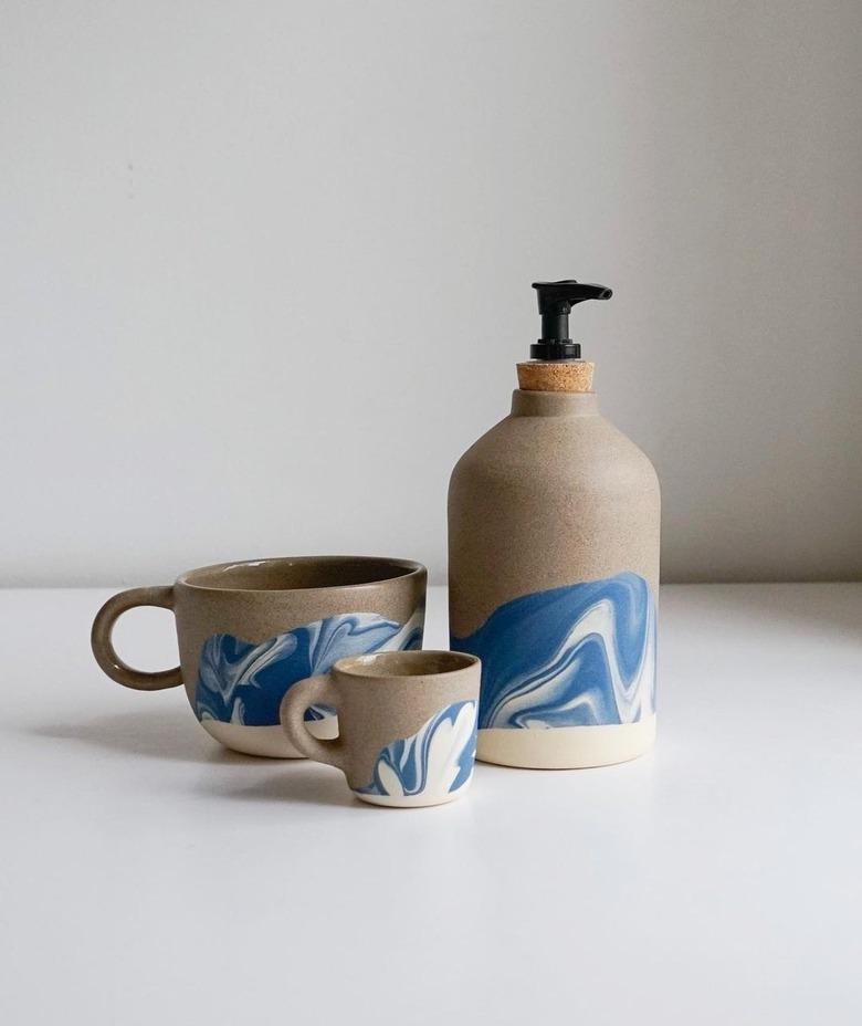 A mug, a smaller cup, and a ceramic soap dispenser with a beige base and blue accents on a white surface.