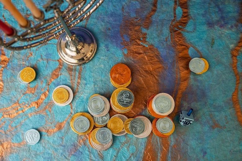 Image from above of assorted Hanukkah gelt on a colorful table next to a menorah.