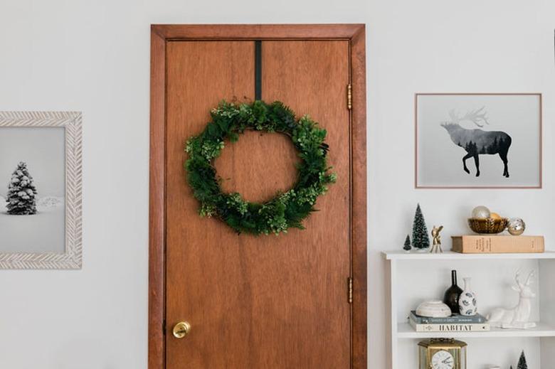 Faux evergreen Christmas wreath on wood door with framed art and white bookshelf