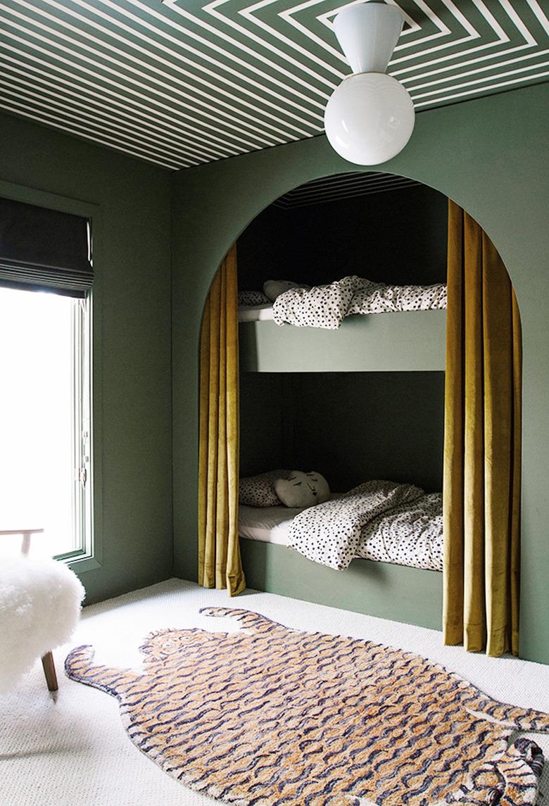 Kids' minimalist bedroom with green walls, tiger area rug, and modern ceiling light