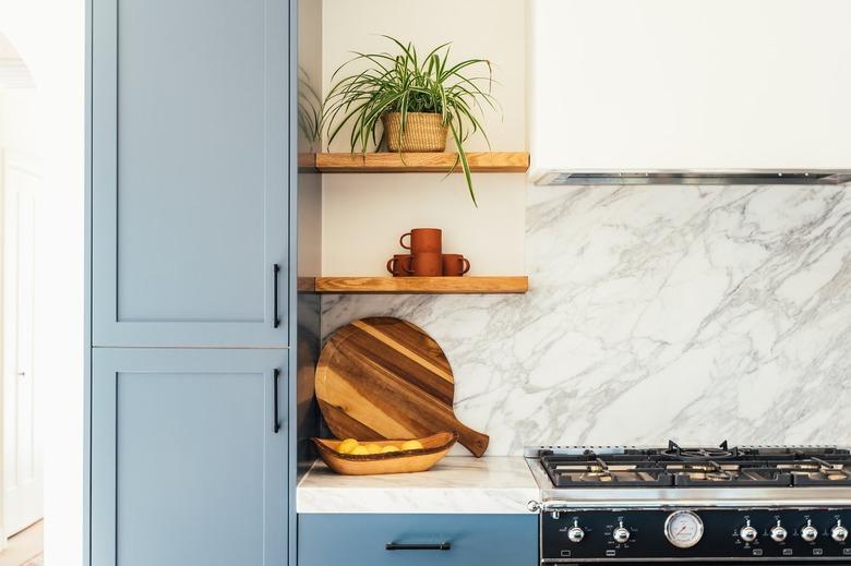 Kitchen with blue cabinets and black hardware, with white marble backsplash over stove