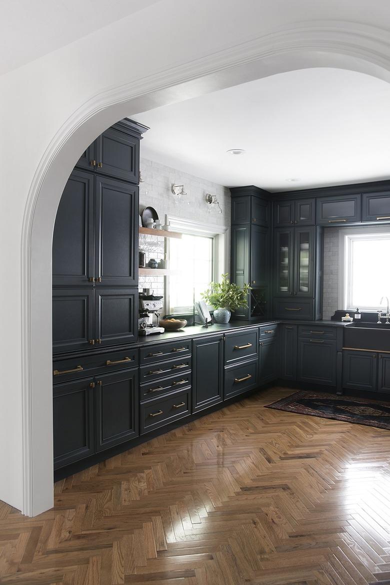 Kitchen with herringbone wood floors, dark cabinets and floating shelves.