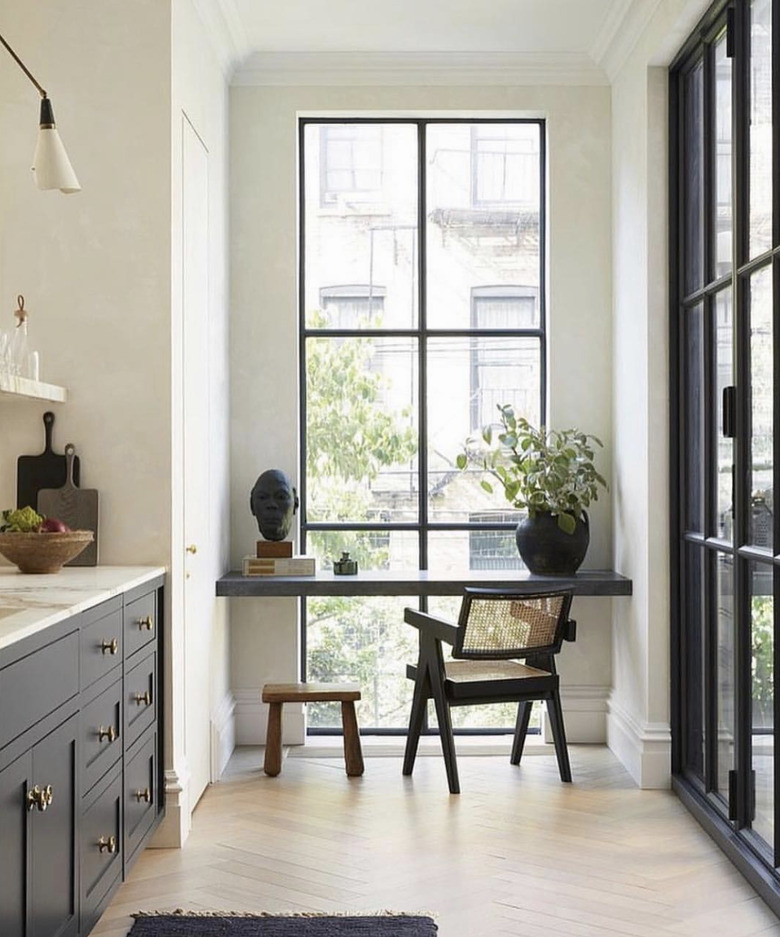 Kitchen nook idea with galley kitchen with black cabinets, marble countertops, a floor-to-ceiling window at one end, and a built-in desk at the window.