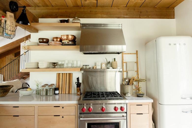 A kitchen with a retro white fridge, wood shelves, wood cabinets, and a red knob stove.