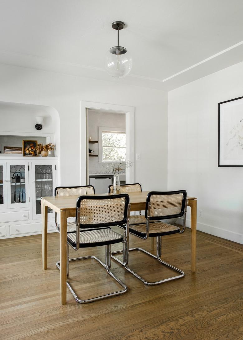 Minimalist dining room with a globe pendant light, wood and cane dining furniture, built-in cabinets.