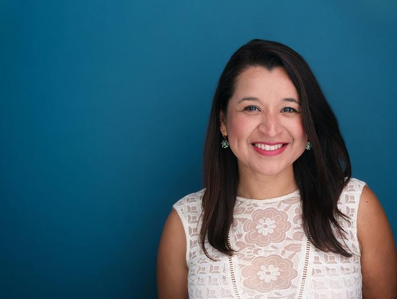 person with long black hair and white shirt against a teal background