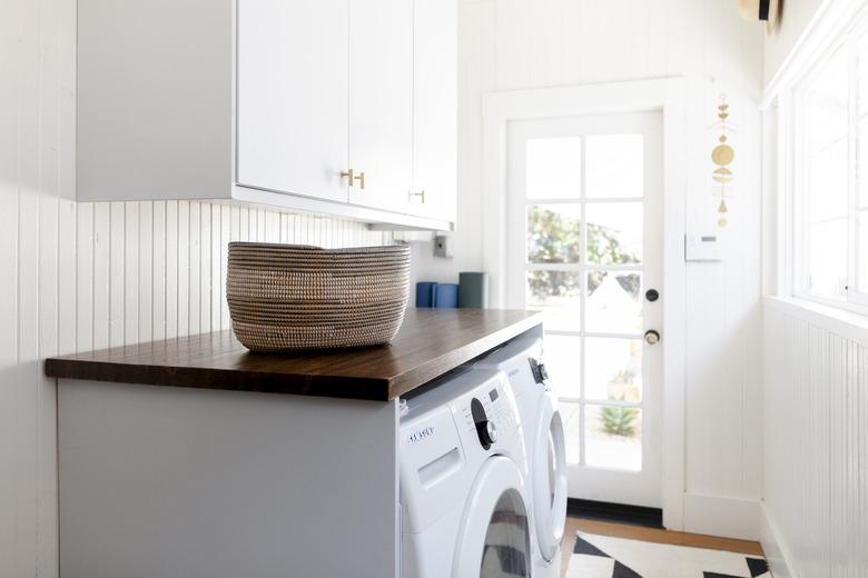 white laundry room idea with wood countertop over appliances and rug on the floor