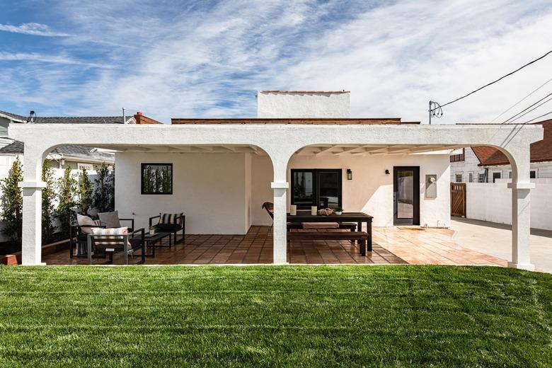 A Spanish-style home's backyard with a covered porch and a lush green lawn