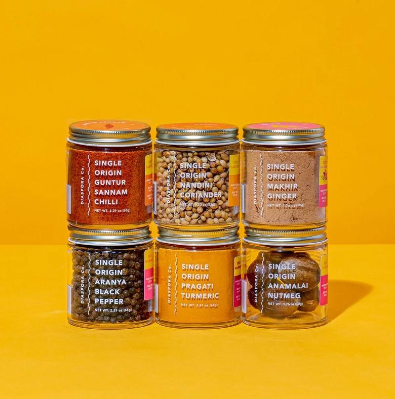 A collection of six Diaspora Co. spices stacked together in two rows. Their labels read Pragati Turmeric Aranya Black Pepper, Guntur Sannam Chillies, Anamalai Nutmeg, Nandini Coriander, and Makhir Ginger.