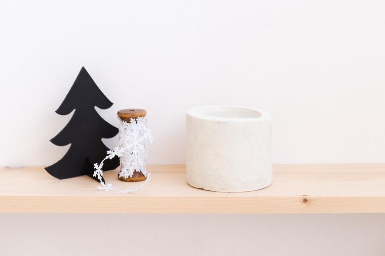 DIY concrete candle on wooden ledge next to snowflake string and Christmas tree toy against white background