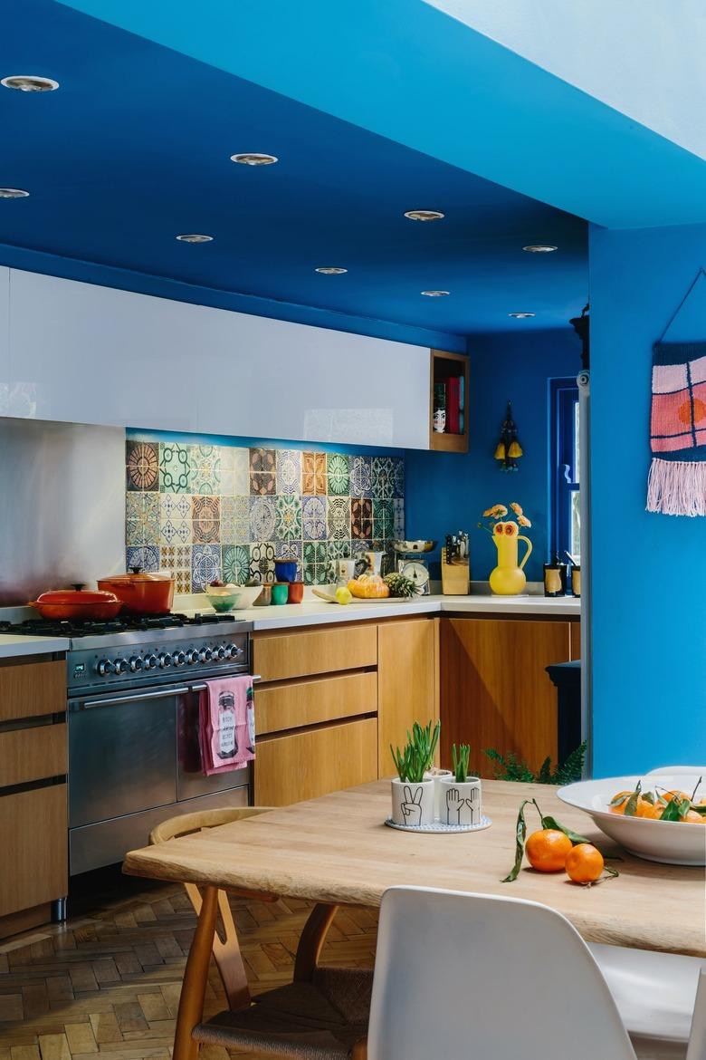 blue walls in maximalist kitchen with wood cabinets and patterned tile backsplash