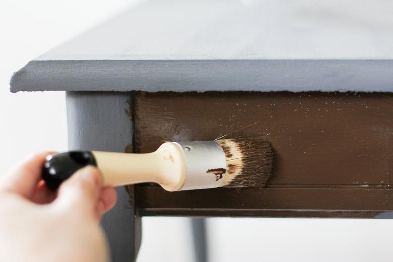 Hand painting brown product onto side face of grey side-table against white background