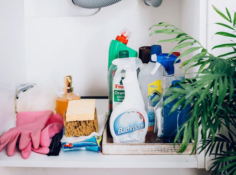 cleaning product bottles, sponges, and pink rubber gloves underneath bathroom sink