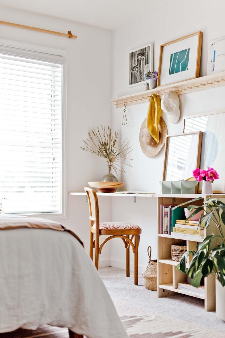 white minimalist home office with wooden desk and hanging shelf above it with art. Palms in vases