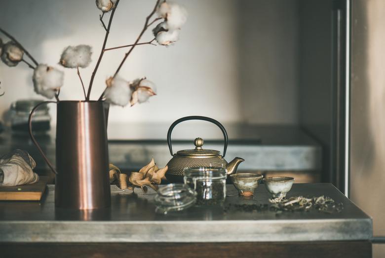 Golden teapot and cups full of tea on concrete counter