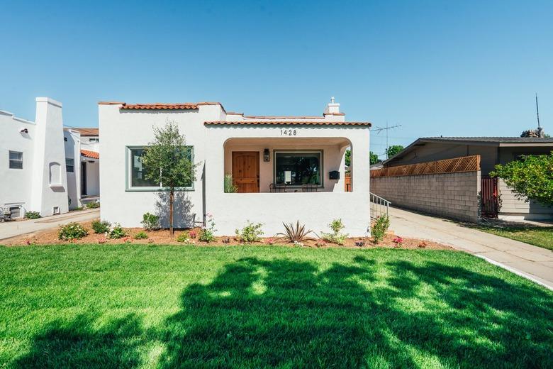 A front lawn of a Spanish style white house with terra-cotta roof tiles