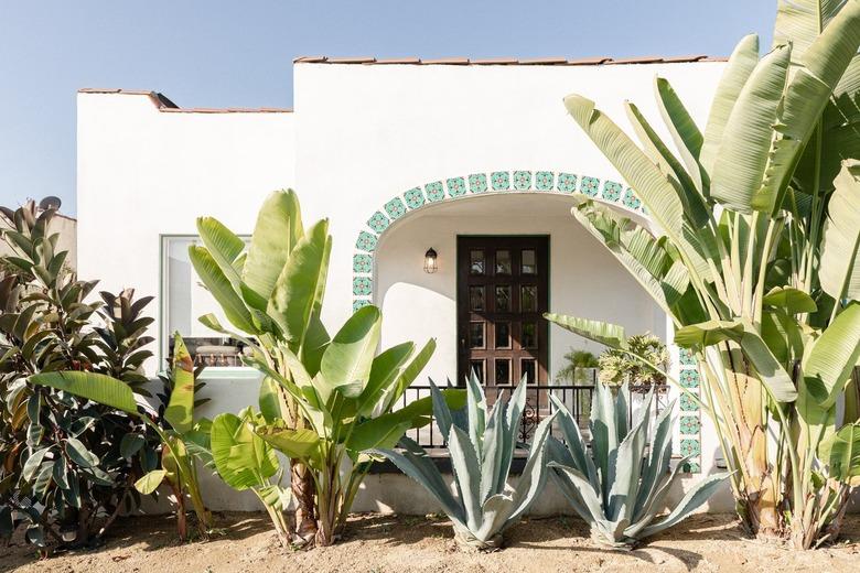 A white Spanish-style home surrounded by tall green plants