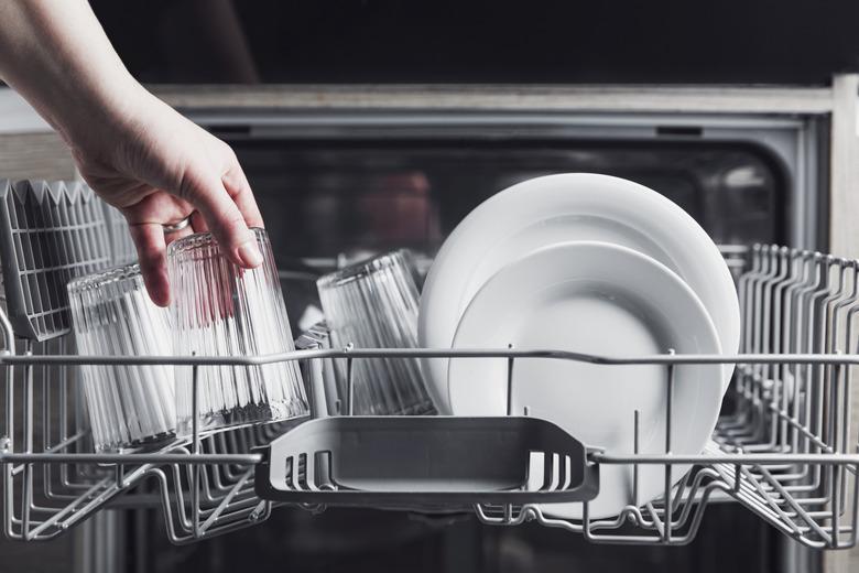 Open dishwasher with clean cutlery, glasses, dishes inside home kitchen.