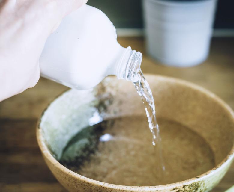 a clear liquid such as rubbing alcohol being poured into a light brown ceramic bowl