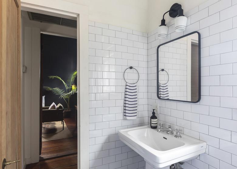 bathroom with white subway tile wall, black square mirror, black light fixture, pedestal sink, black and white striped hand towel