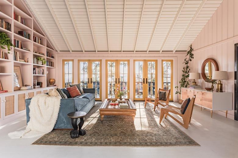 A-frame living room with built-in bookcases, pink walls, earthy furniture, yellow French doors, and eclectic decor.