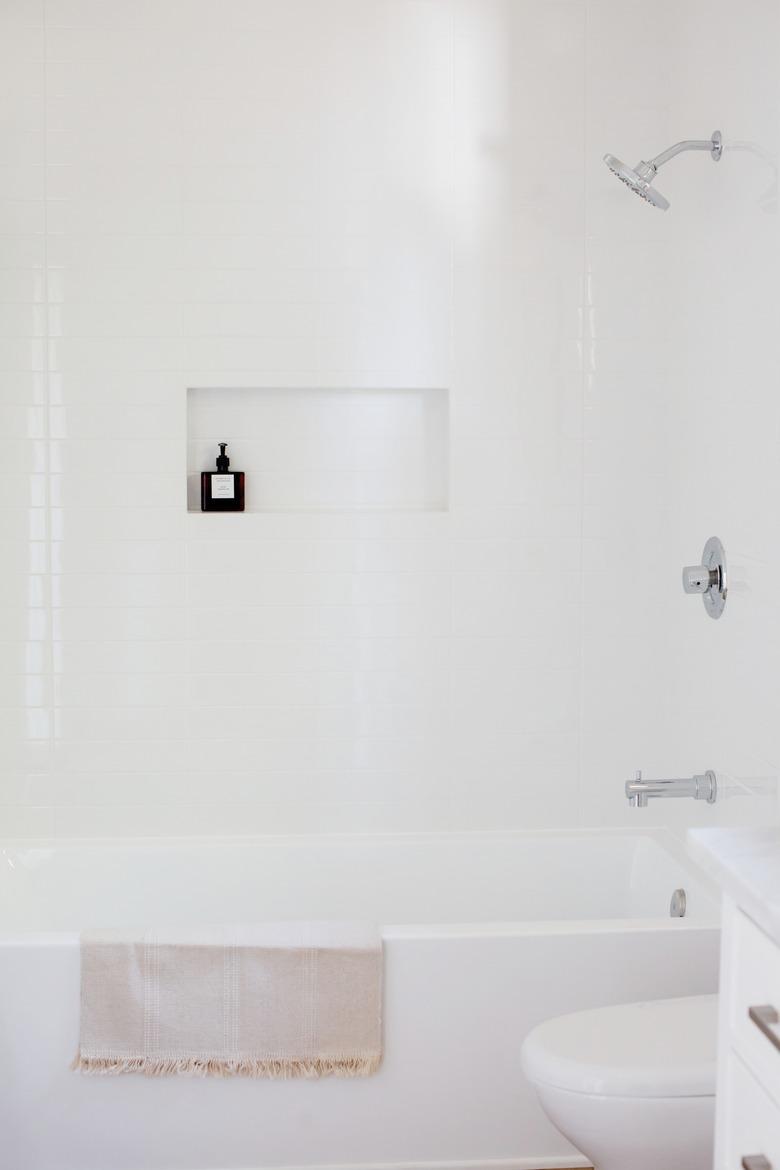 white tub with a fringed towel draped over, white shower wall