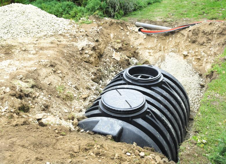 A black septic tank halfway buried in dirt outside