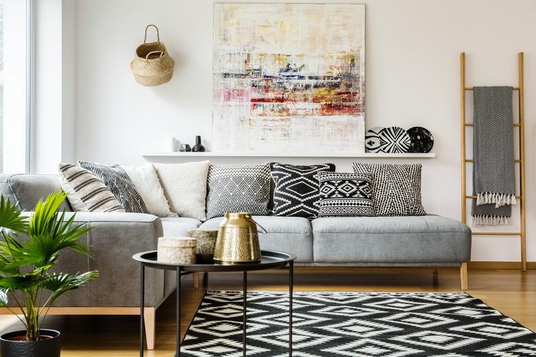 Patterned pillows on gray corner sofa in living room interior with table and painting. Real photo.