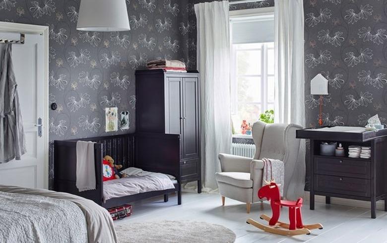 Nursery with gray wallpaper, black crib, changing table, bed, curtains.