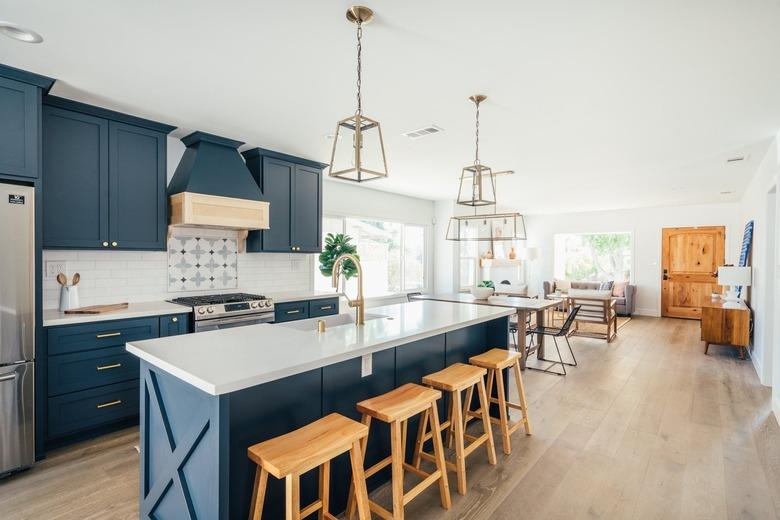 Kitchen with dark blue cabinets, kitchen island with wood stools, and gold lantern pendant lights