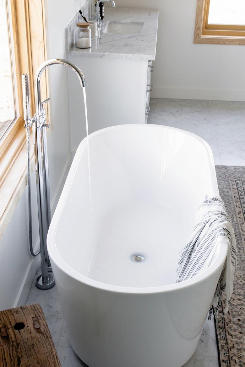 white freestanding tub with water flowing from floor-mount silver faucet, striped towel draped over the side, area rug, bathroom vanity with marble counters