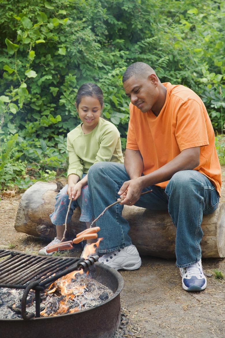 Father and daughter roasting hot dogs in camp fire