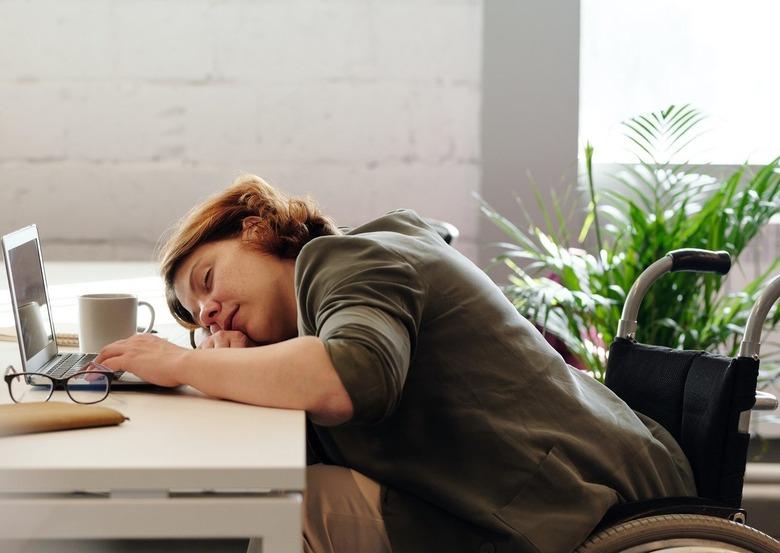 woman with wheelchair sleeping at desk with laptop