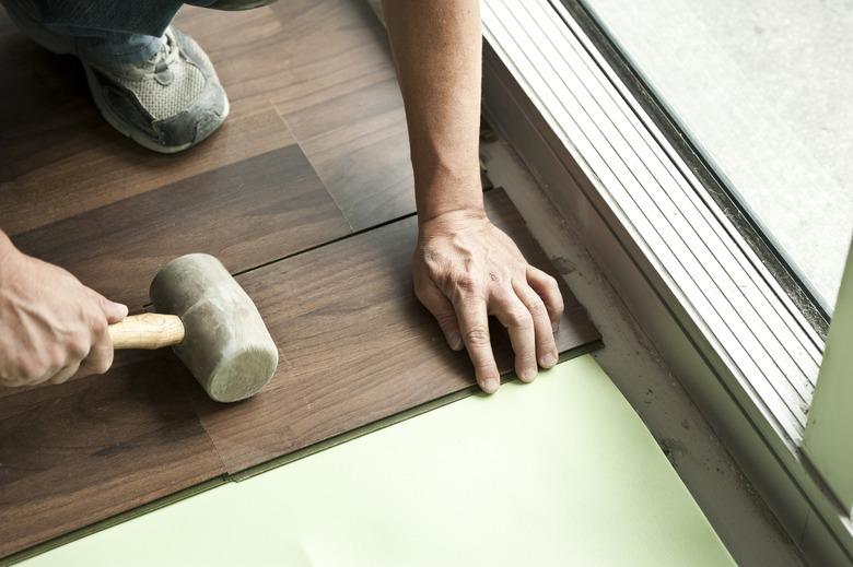 Two male hands holding mallet installing hardwood floor.