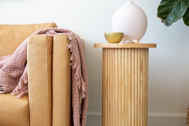 Fluted side table with dowel base, birch circle board tabletop, round pink vase and gold bowl, neutral sofa and pink blanket