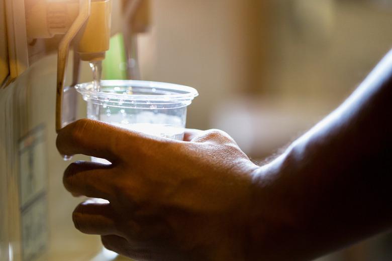 Male hand serving water of a water cooler in plastic cup.