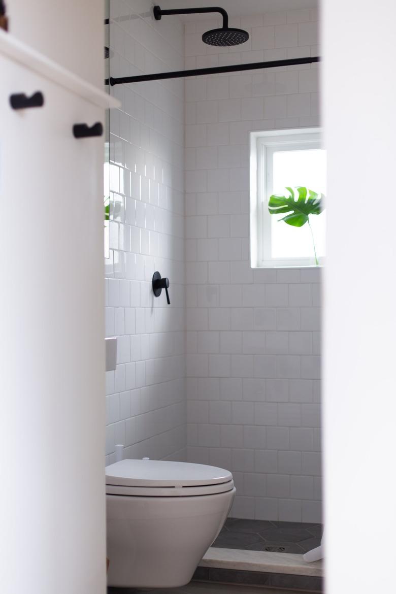 White subway tile bathroom with white toilet and shower window with monstera leaf