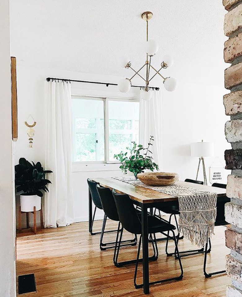 Minimal dining room with metal and wood table and black leather industrial chairs, white globe chandelier, and white midcentury floor planter