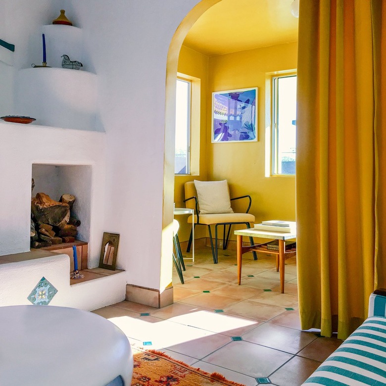 Modern Spanish-style room with white fire alcove in living room, yellow side room with chairs, and white and green tiling