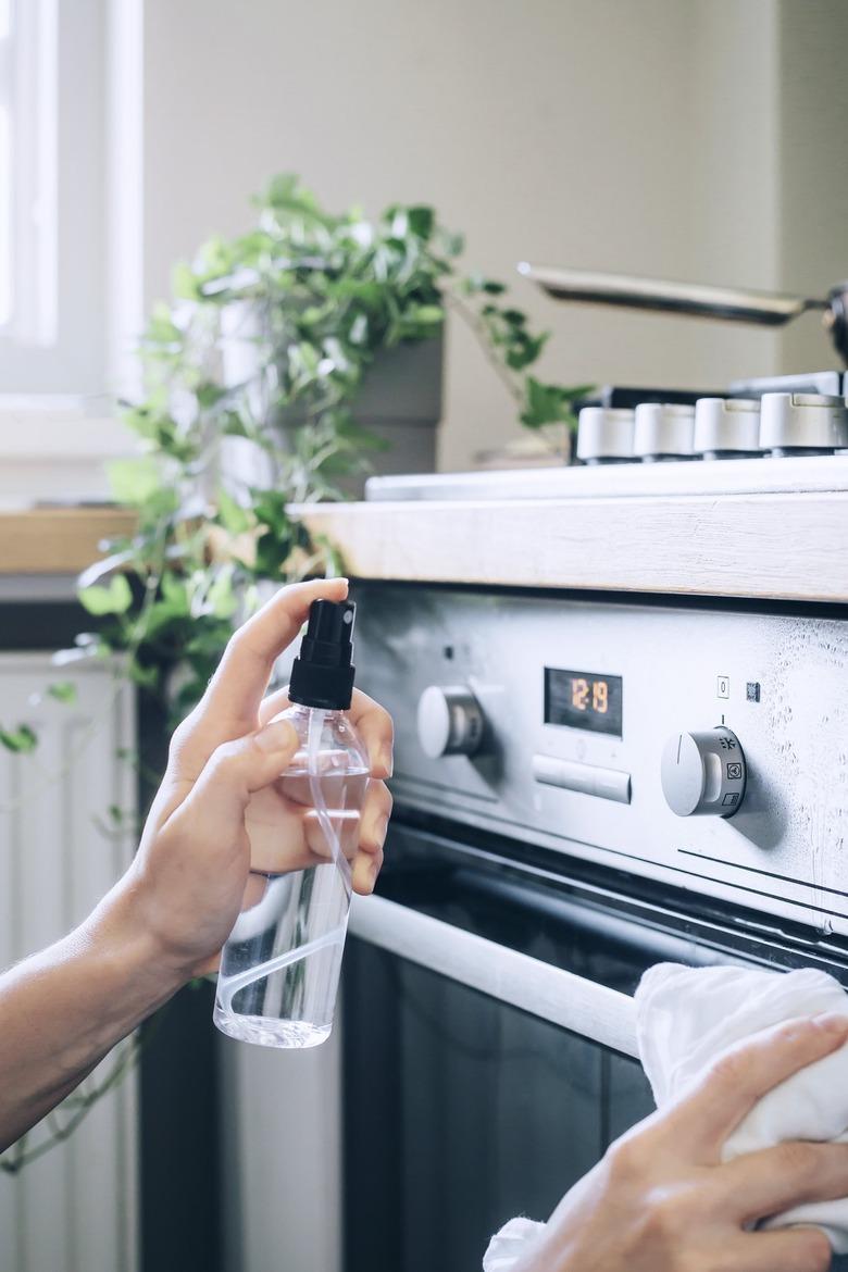 using spray bottle to clean a stainless steel oven with water and rubbing alcohol