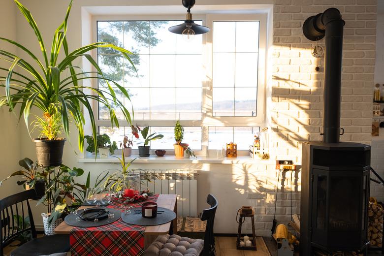 Sunny interior of a loft-style house with potted plants, a large window, a covered table for the Christmas and New Year holidays