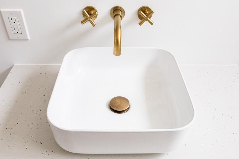 white ceramic vessel sink, gold stopper and faucet, wall outlet