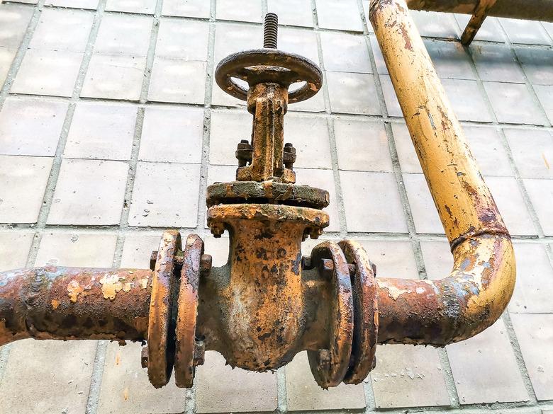 Old rusty iron pipe and control valve on house wall